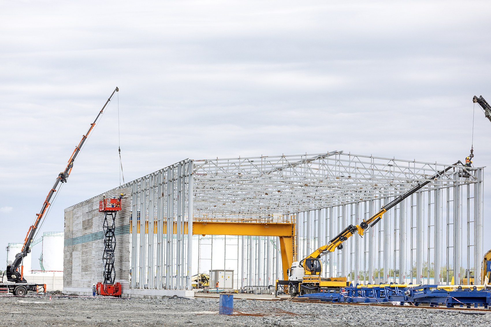 Mobile hydraulic crane lifting a pre-assembled structural steel portal frame rafter during warehouse erection