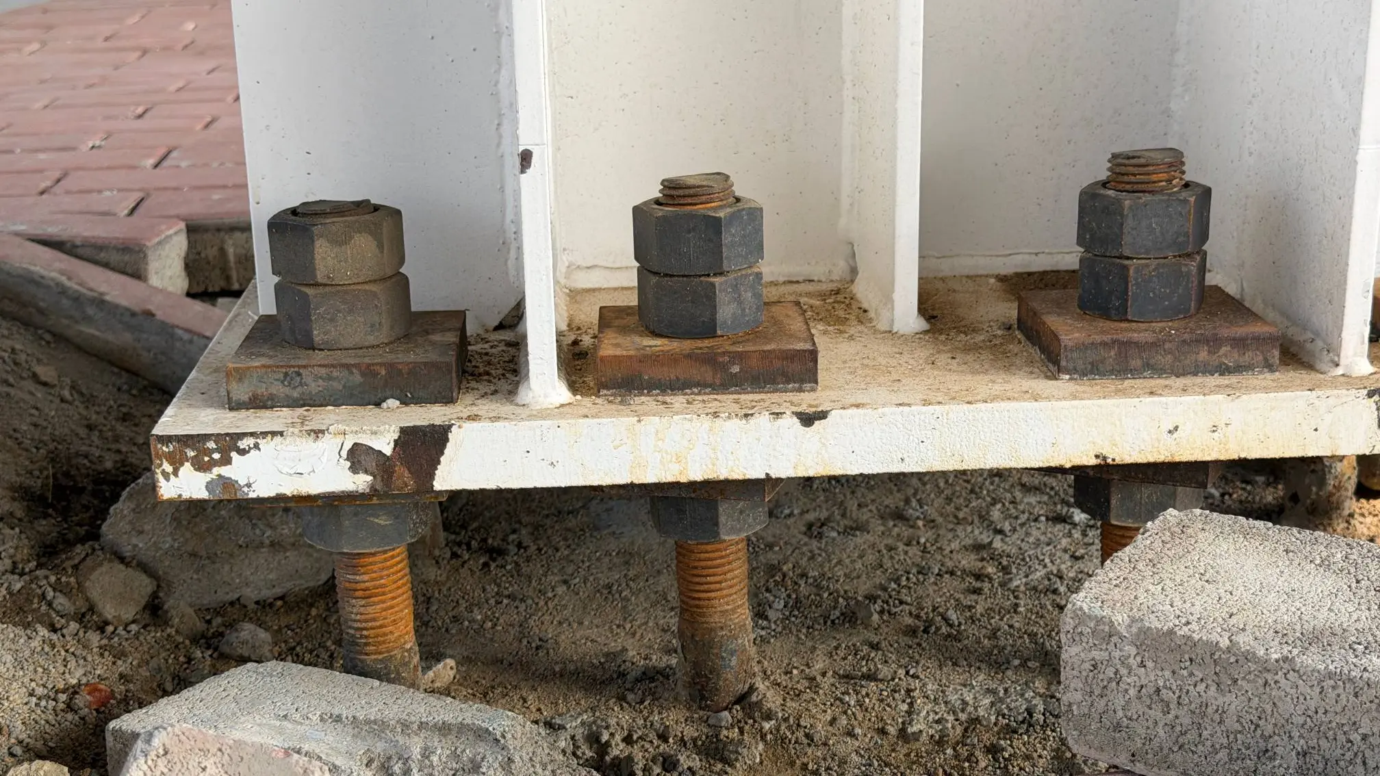 Structural steel column baseplate resting on concrete pedestal with heavy anchor bolts and leveling nuts.