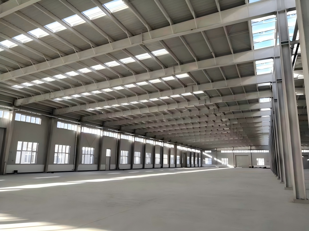 Clear-span structural steel warehouse frame integrated with concrete tilt-up wall panels showing slotted deflection clips and perimeter columns
