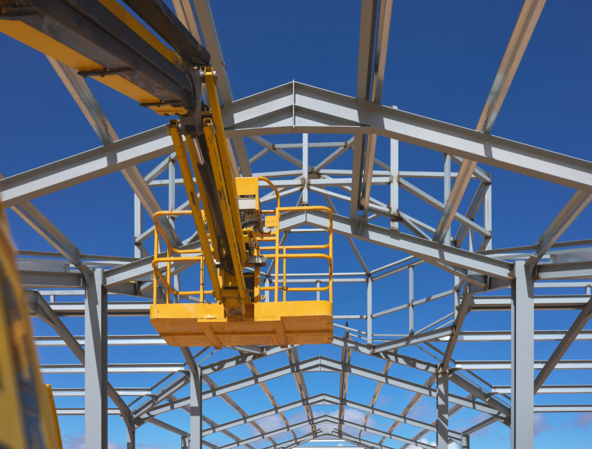 Heavy pre-engineered structural steel warehouse framework during erection with mobile crane and bolted portal rafter connections.